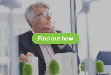A serious, middle-aged man wearing a suit and glasses is looking off into the distance, with his hand resting on his chin in a pensive pose. He is indoors, seemingly in an office, with some blurred greenery or model buildings in the foreground. Overlaid in large white text are the words "VEU HOT WATER REBATES FOR VICTORIAN BUSINESSES" with a green call-to-action button beneath reading "Find out how".