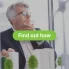 A serious, middle-aged man wearing a suit and glasses is looking off into the distance, with his hand resting on his chin in a pensive pose. He is indoors, seemingly in an office, with some blurred greenery or model buildings in the foreground. Overlaid in large white text are the words "VEU HOT WATER REBATES FOR VICTORIAN BUSINESSES" with a green call-to-action button beneath reading "Find out how".