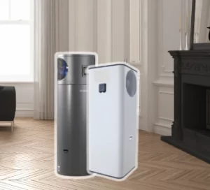 Two large, vertical indoor heat pump water storage tanks—one dark gray and one white—in a room with a wooden floor.