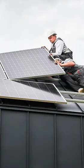 Two installers working to lift and mount solar panels onto a dark roof.