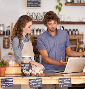 Two baristas/cafe workers looking at a laptop behind the counter.