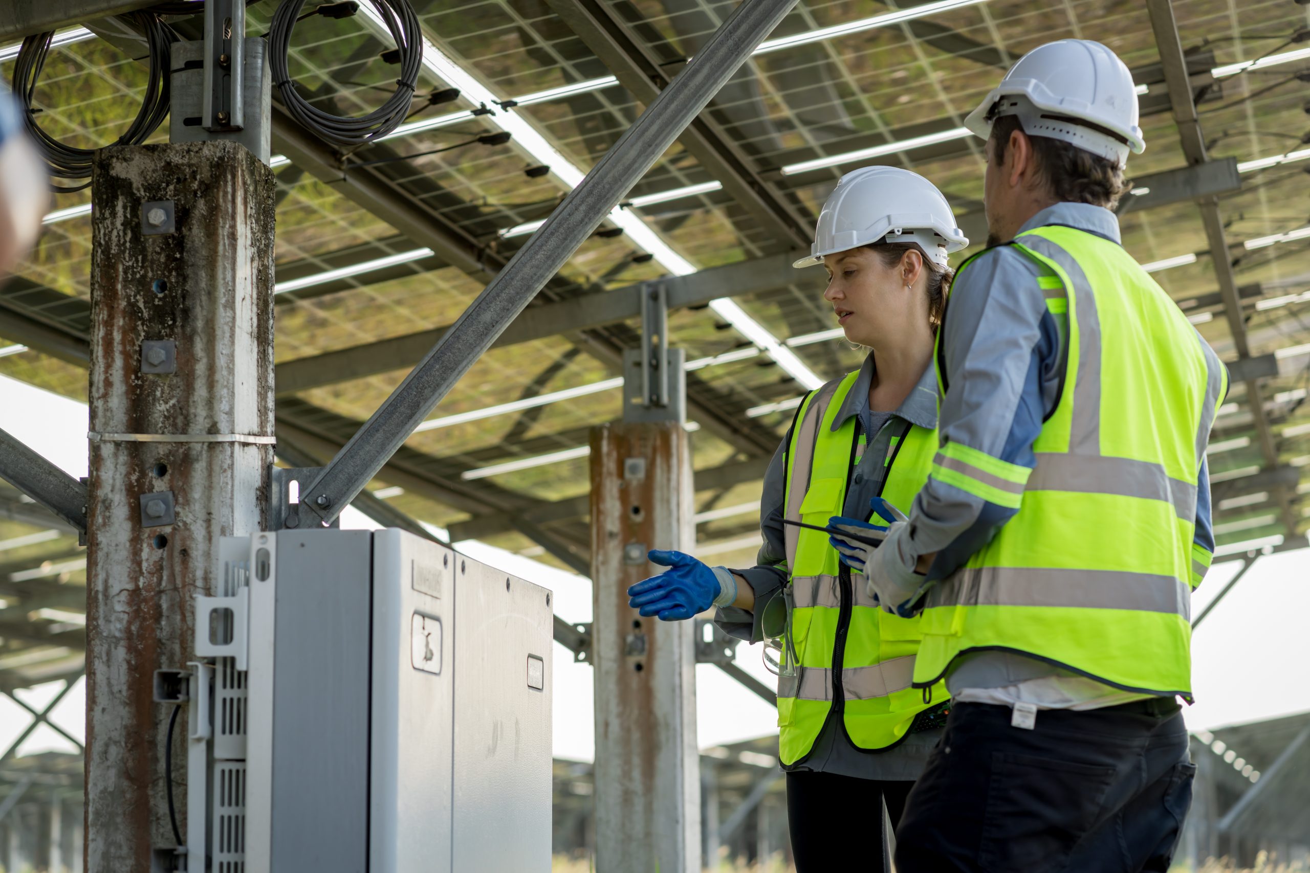 Two engineers in hard hats and high-visibility vests inspecting equipment at a solar farm.