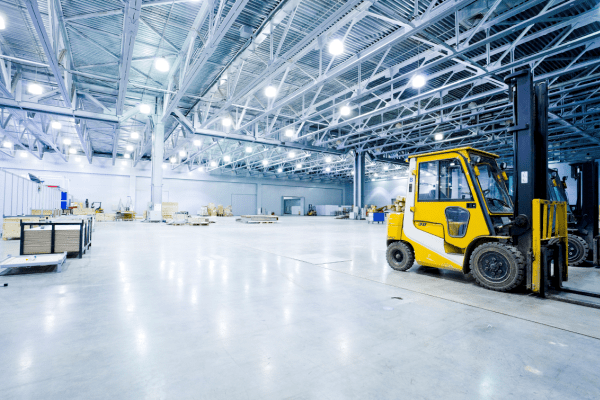 Interior of a large, brightly lit, clean industrial warehouse with a yellow forklift in the foreground.